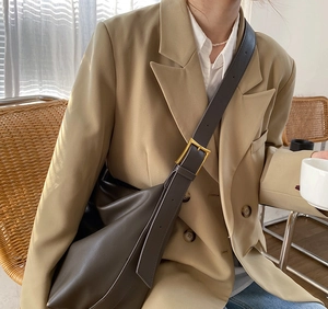 Deep brown leather hobo bag with a wide strap and gold buckle shown on a model