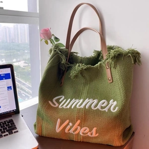 Detail of woven straw tote bag featuring Summer Vibes embroidery and brown leather handles