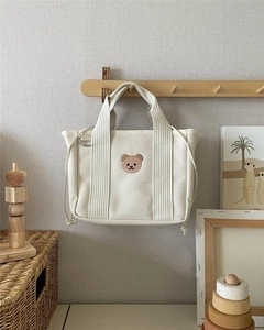 Close-up of cream canvas mommy bag with bear embroidery hanging on a wooden rack