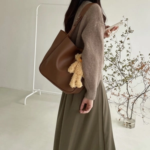 Brown tote bag with plush bear charm shown on model in a minimalist lifestyle setting