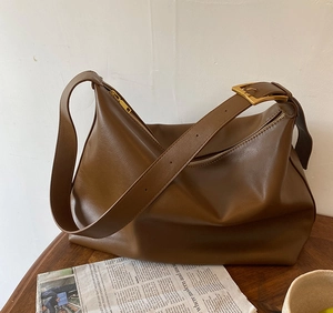 Close-up of brown leather hobo bag with adjustable gold buckle on a wooden table