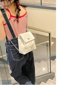 Vue arrière d'un mannequin portant un mini sac à dos blanc perle avec chaîne sur l'escalier