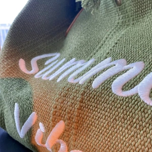 Close-up of green woven fabric texture with white Summer Vibes 3D embroidery detail