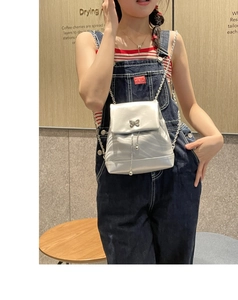 Détail d'un sac à dos argenté avec fermoir papillon et chaîne porté par un mannequin