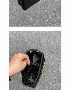 Detail view of black litchi leather texture, golden twist lock, and zip inner pocket