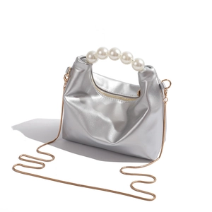 Detail of silver metallic dumpling bag featuring pearl handle and golden chain strap