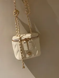 Close-up of quilted cream mini box bag with gold camellia hardware and chain strap
