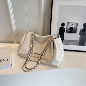 Close-up of cream leather tote bag with silver chain strap and metal pendant detail