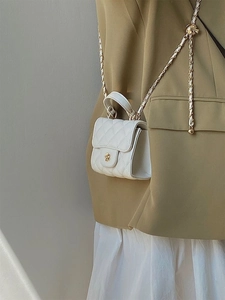 Dettaglio mini borsa trapuntata bianca con fibbia a fiore dorata su blazer kaki