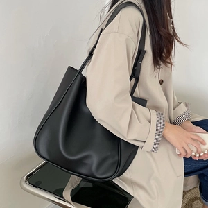 Large black leather tote bag with adjustable strap worn by model in a stylish trench coat