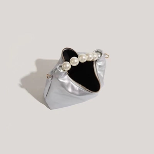 Close-up of silver mini dumpling bag with faux pearl handle and gold zipper detail