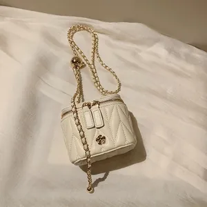 Close-up of beige quilted mini box bag with dual zipper and golden camellia floral hardware