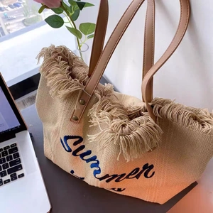 Close-up of embroidered Summer text and long fringe tassels on straw tote bag