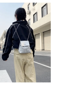 Sac à dos argenté avec chaîne, fermoir papillon et texture satinée élégante