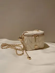 Detailed close-up of quilted cream mini bag with gold camellia logo and chain strap
