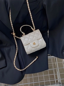 Dettaglio mini borsa trapuntata crema con chiusura a camelia dorata su blazer