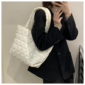 Close-up of a white quilted tote bag featuring a padded down texture and wide shoulder strap