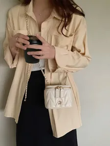 Detail of white quilted mini vanity bag featuring gold camellia hardware and chain strap