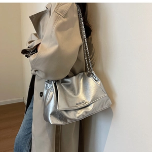 Close-up of shiny silver wrinkled tote bag with metal chain strap worn by a model