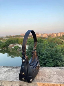 Détail du sac hobo en cuir noir avec clous étoiles argentés sur fond naturel extérieur
