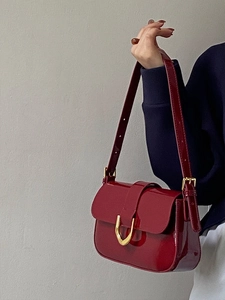 Gros plan d'un sac à bandoulière en cuir verni bordeaux avec boucle fer à cheval dorée