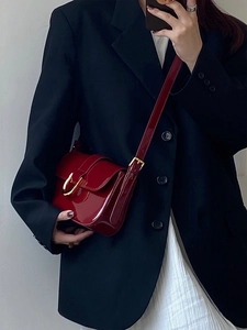 Détail du sac à bandoulière en cuir verni rouge avec une boucle fer à cheval dorée