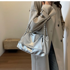 Silver metallic shoulder bag with thick chain strap shown on a model in trench coat