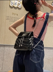 Gros plan du mini sac à dos en cuir verni noir avec chaîne et nœud métallique sur modèle