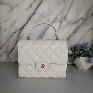 Dettaglio di una borsa trapuntata bianca con chiusura girevole a forma di camelia dorata