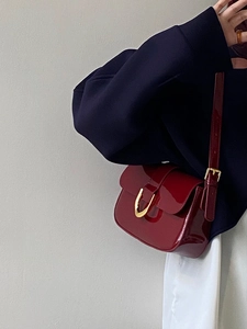 Gros plan du sac en cuir verni bordeaux avec finition brillante et boucle dorée en forme de U
