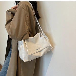 Detail of cream white faux leather shoulder bag with silver chain strap on trench coat