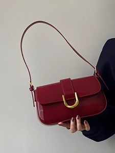Détail du sac en cuir verni bordeaux avec boucle fer à cheval dorée et finition brillante