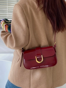 Détail du sac en cuir verni bordeaux avec boucle fer à cheval dorée et manteau beige