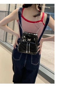 Détail d'un mini sac à dos en cuir verni noir avec nœud argenté et bretelles chaîne