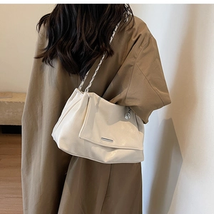 Detail of off-white pleated tote bag with silver chain strap worn by a model