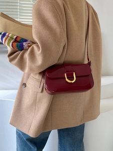 Gros plan sur le sac bandoulière rouge vin brillant avec sa boucle dorée en fer à cheval