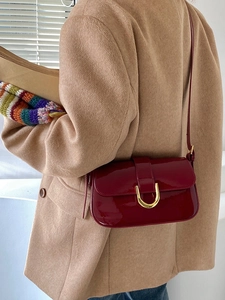 Détail du sac en cuir verni bordeaux avec boucle fer à cheval sur un manteau beige