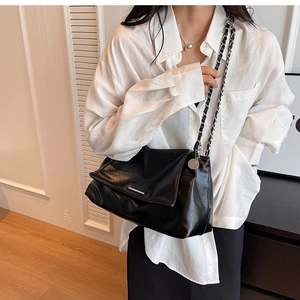 Detail of glossy black leather flap bag with silver hardware and chain strap on a model