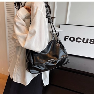 Close-up of black glossy faux leather shoulder bag featuring silver chain and metal trim