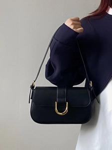 Détail d'un sac porté épaule en cuir noir avec boucle fer à cheval dorée et bandoulière