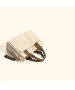 Detail of off-white canvas tote bag with brown straps and functional front pockets
