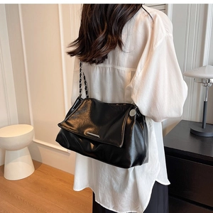 Detail of black faux leather shoulder bag featuring silver metal bar and chain strap texture