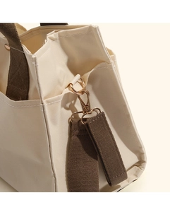Detail view of gold lobster clasp on ivory canvas bag with brown fabric strap