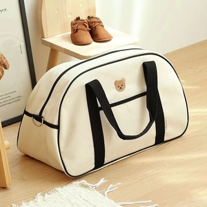 Detailed view of beige canvas mommy bag with brown bear embroidery and sturdy black handles