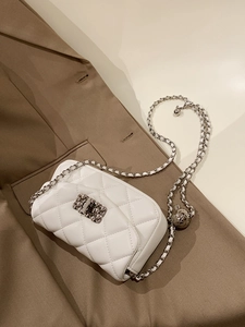 Close-up of white quilted chain bag with silver ball adjuster on a brown blazer