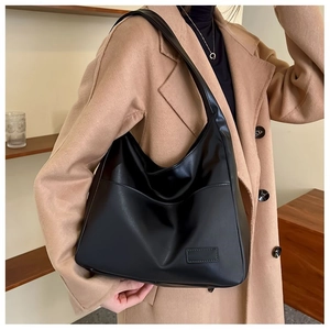 Detail of a large black matte leather hobo bag worn with a wool coat for a chic look