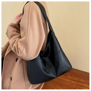 Detail of minimalist black soft leather tote bag worn with a camel wool coat
