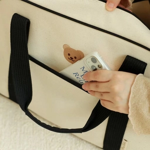 Close-up of the front pocket on the bear embroidered canvas tote bag storing a smartphone