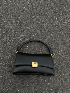 Dettaglio borsa in pelle lucida nera con fibbia dorata curva e anello del manico