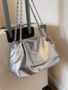 Silver metallic tote bag with chain strap displayed on a white suitcase for travel